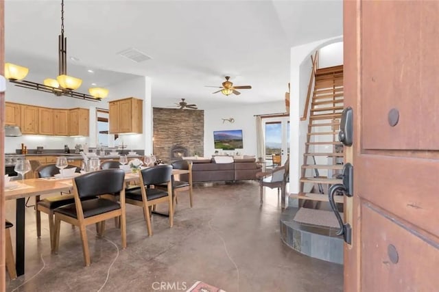 dining room with ceiling fan, a stone fireplace, and concrete flooring