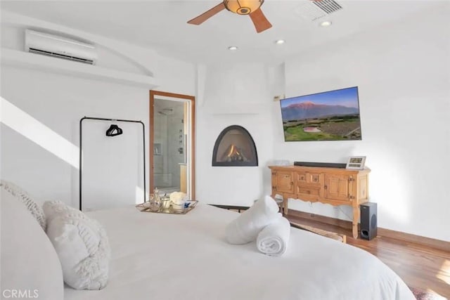 bedroom with a wall unit AC, ceiling fan, ensuite bathroom, and wood-type flooring