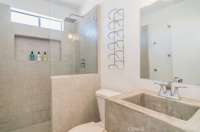 bathroom with tiled shower, toilet, and sink