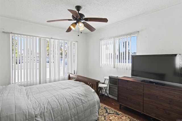 bedroom with a textured ceiling, ceiling fan, dark wood-type flooring, and multiple windows