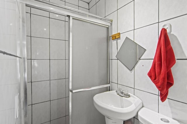 bathroom featuring an enclosed shower, toilet, tile walls, and sink