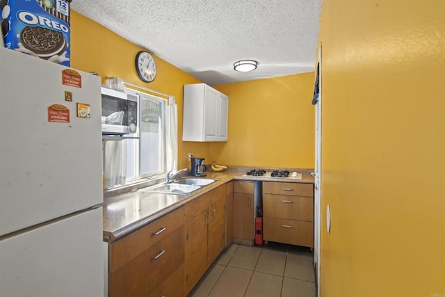 kitchen featuring white cabinets, white refrigerator, sink, light tile patterned floors, and a textured ceiling