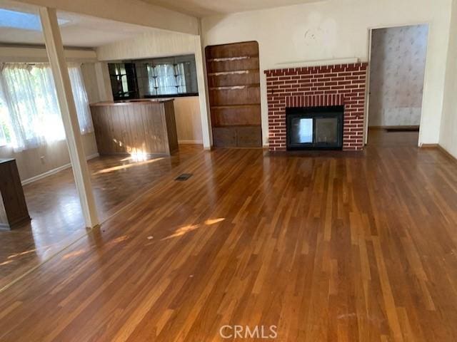 unfurnished living room with baseboards, a brick fireplace, and wood finished floors