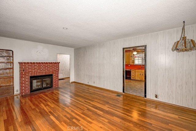 unfurnished living room featuring visible vents, a textured ceiling, a brick fireplace, and wood finished floors