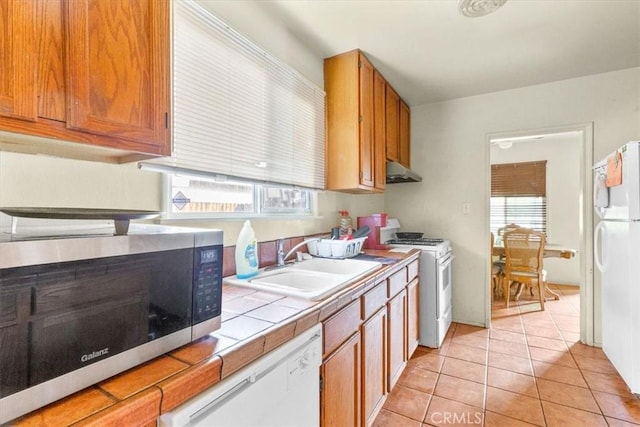 kitchen with tile counters, light tile patterned floors, white appliances, and sink