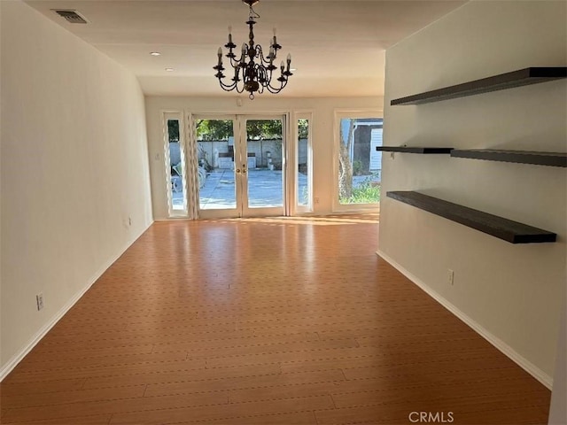 empty room featuring an inviting chandelier, wood-type flooring, and french doors