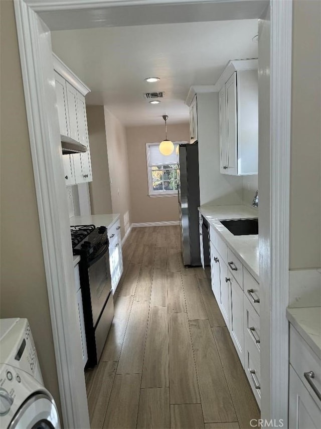 kitchen featuring black range oven, sink, hardwood / wood-style floors, white cabinetry, and stainless steel refrigerator