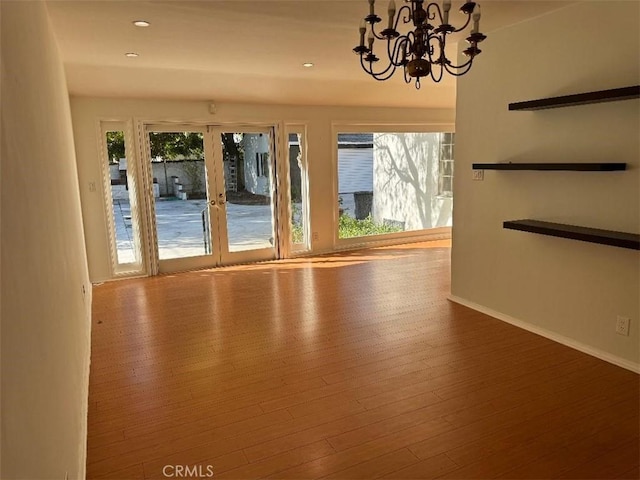 unfurnished room featuring a chandelier, wood-type flooring, french doors, and plenty of natural light