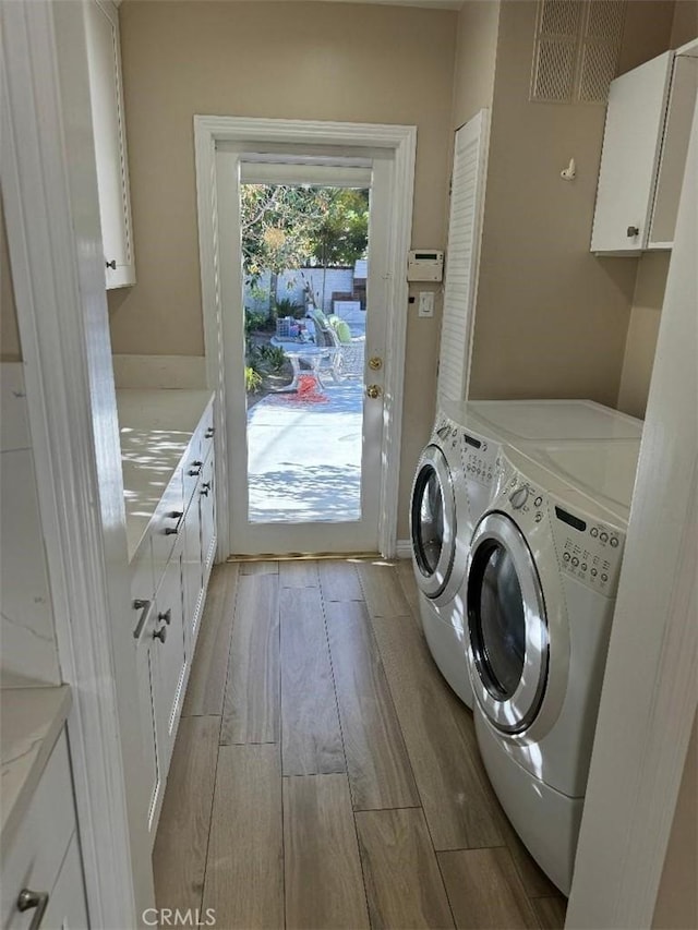 washroom with separate washer and dryer, cabinets, and light wood-type flooring