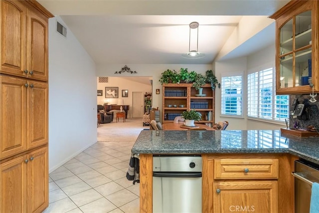 kitchen with dark stone counters, vaulted ceiling, stainless steel dishwasher, light tile patterned floors, and decorative light fixtures