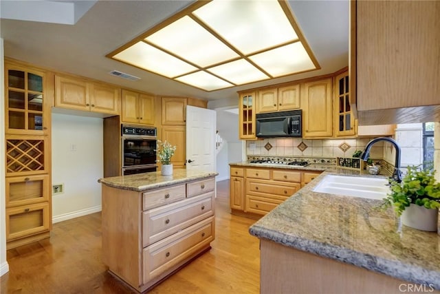 kitchen featuring sink, tasteful backsplash, light stone counters, light hardwood / wood-style flooring, and black appliances