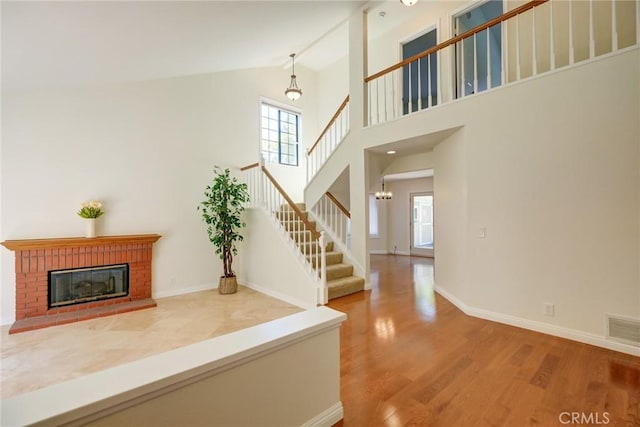 interior space featuring a brick fireplace, hardwood / wood-style flooring, high vaulted ceiling, and a notable chandelier