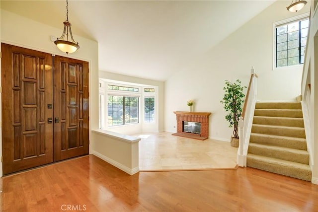 foyer entrance featuring hardwood / wood-style floors, a healthy amount of sunlight, a brick fireplace, and vaulted ceiling