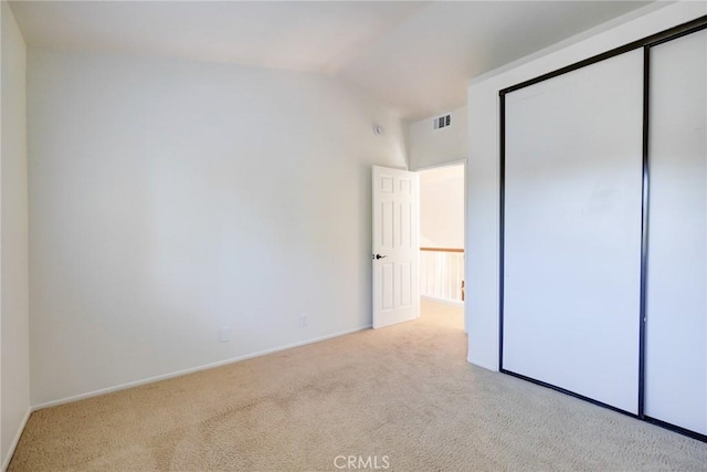 unfurnished bedroom with vaulted ceiling, light carpet, and a closet