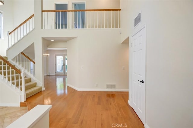 interior space featuring light hardwood / wood-style floors, a towering ceiling, and an inviting chandelier