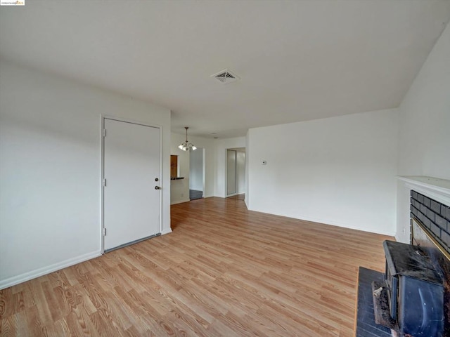 unfurnished living room with a brick fireplace, light hardwood / wood-style floors, and a notable chandelier