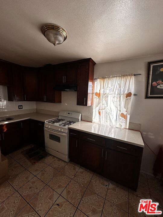 kitchen featuring backsplash, white gas range, dark brown cabinets, a textured ceiling, and sink