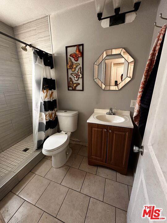 bathroom with tile patterned floors, vanity, toilet, and curtained shower