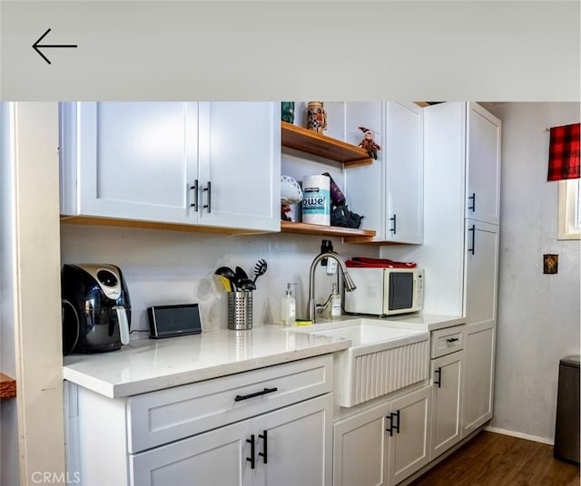 bar with light stone counters, white cabinetry, dark wood-type flooring, and sink