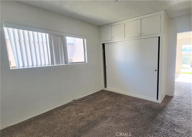 unfurnished bedroom with multiple windows, a textured ceiling, dark carpet, and a closet