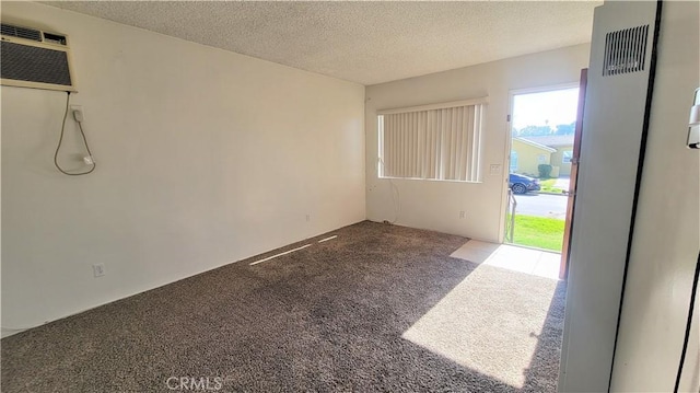 carpeted empty room with a wall unit AC and a textured ceiling