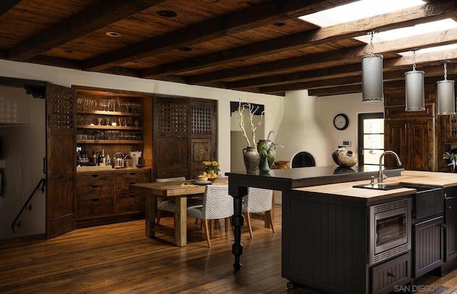 bar featuring stainless steel microwave, sink, hanging light fixtures, and dark hardwood / wood-style floors