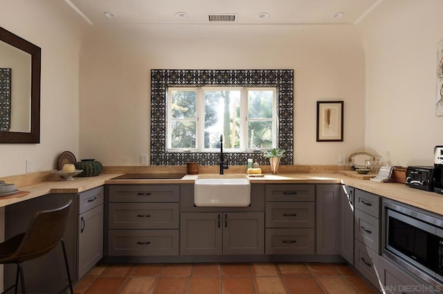 kitchen featuring butcher block counters, stainless steel microwave, sink, gray cabinets, and light tile patterned flooring