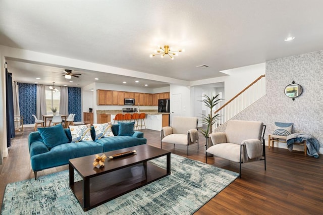 living room with ceiling fan with notable chandelier and dark hardwood / wood-style floors