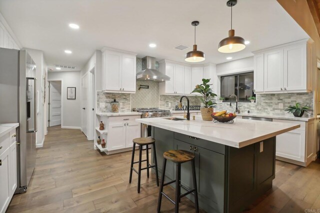 kitchen with wall chimney exhaust hood, white cabinetry, and sink