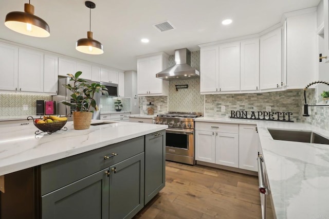 kitchen featuring white cabinets, wall chimney exhaust hood, decorative light fixtures, and appliances with stainless steel finishes