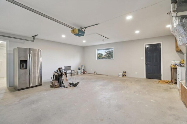 garage with a garage door opener and stainless steel refrigerator with ice dispenser