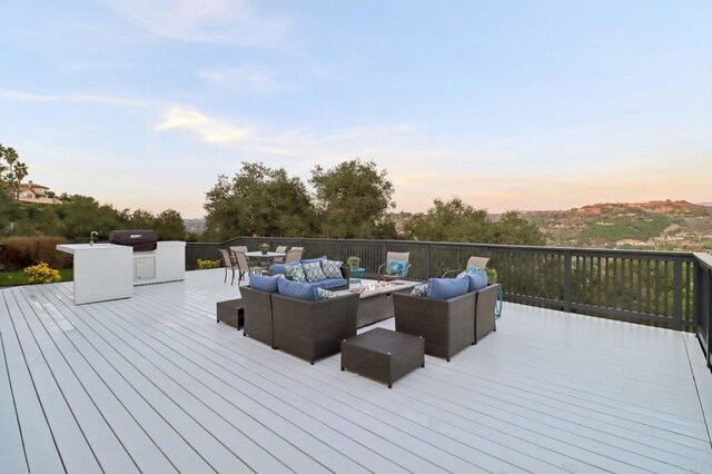 deck at dusk with area for grilling, an outdoor kitchen, and an outdoor hangout area