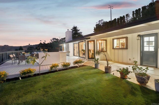 back house at dusk with a yard and a deck