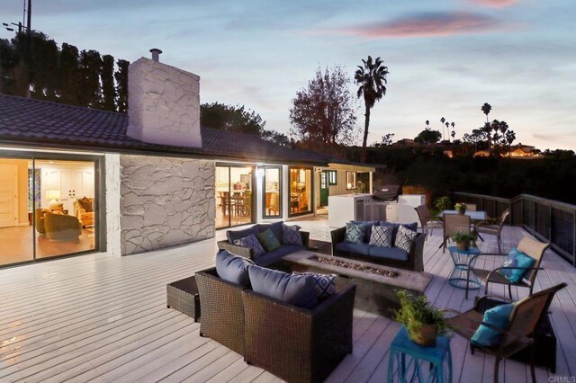 deck at dusk with a grill and an outdoor living space with a fire pit