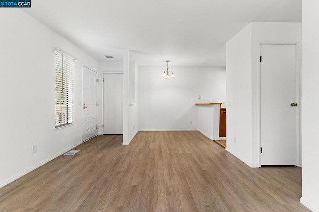 unfurnished room with a notable chandelier and light wood-type flooring