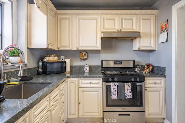 kitchen with cream cabinets, stainless steel gas range oven, dark stone countertops, and sink