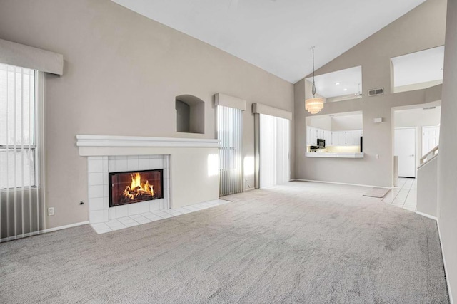 unfurnished living room with a tile fireplace, light carpet, and high vaulted ceiling