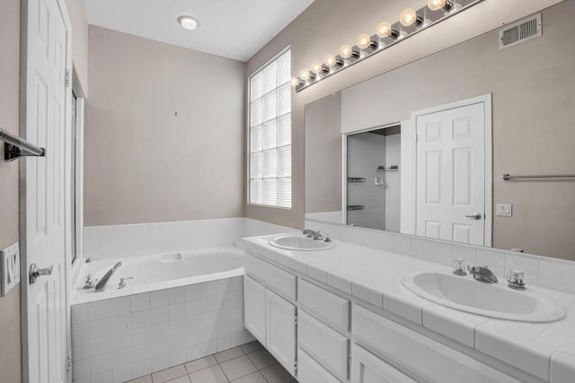 bathroom featuring tile patterned flooring, vanity, and a relaxing tiled tub