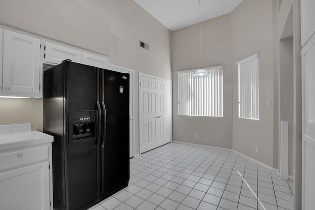 kitchen with tile countertops, black fridge, white cabinetry, and light tile patterned floors