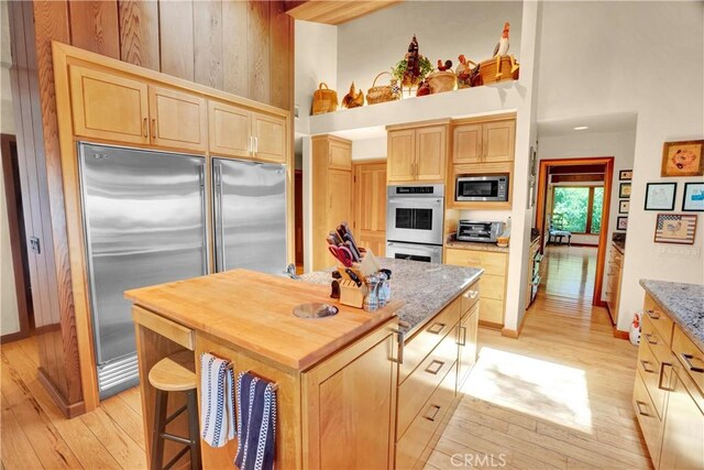 kitchen with light wood-type flooring, light brown cabinets, built in appliances, and a center island