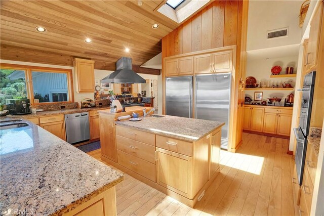 kitchen with light stone counters, light brown cabinets, stainless steel appliances, and a center island with sink