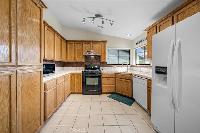 kitchen with white appliances, sink, light tile patterned floors, tile counters, and lofted ceiling