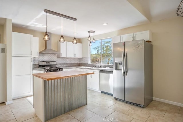 kitchen with a center island, hanging light fixtures, wall chimney range hood, white cabinets, and appliances with stainless steel finishes