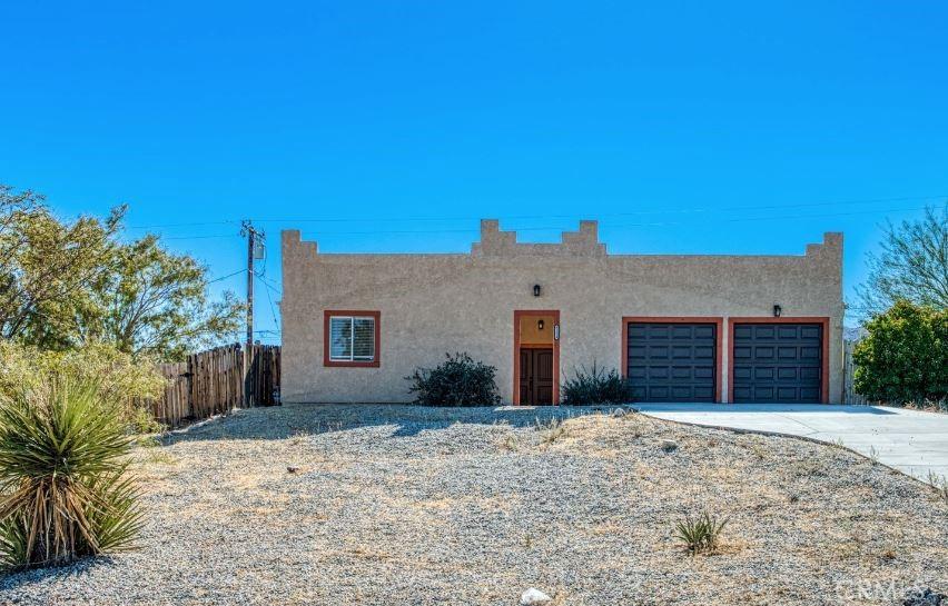 pueblo-style house with concrete driveway, fence, an attached garage, and stucco siding