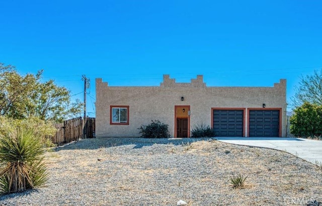 pueblo-style house with concrete driveway, fence, an attached garage, and stucco siding