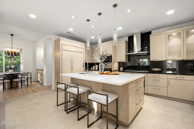 kitchen featuring decorative light fixtures, wall chimney range hood, an island with sink, and black microwave