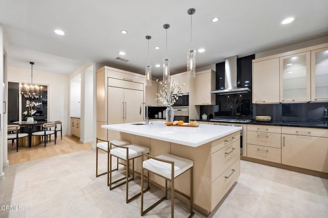 kitchen featuring sink, hanging light fixtures, stainless steel appliances, wall chimney range hood, and a center island with sink