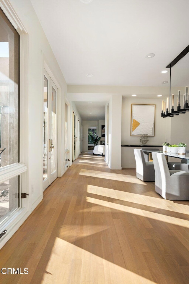 hall with a healthy amount of sunlight, light wood-type flooring, and french doors