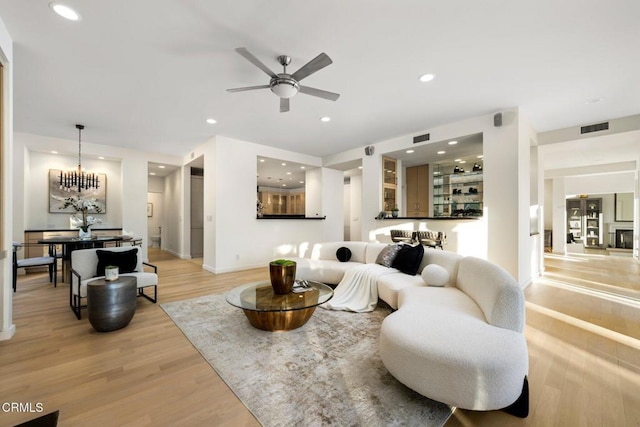 living room featuring ceiling fan with notable chandelier and light wood-type flooring