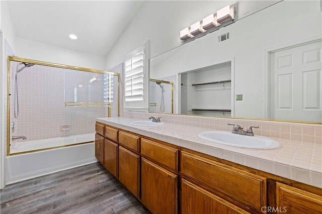 bathroom featuring backsplash, vanity, vaulted ceiling, shower / bath combination with glass door, and wood-type flooring